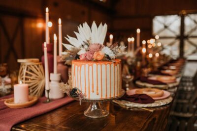 A round white wedding cake with orange frosting running down the sides with candles surrounding it on a table